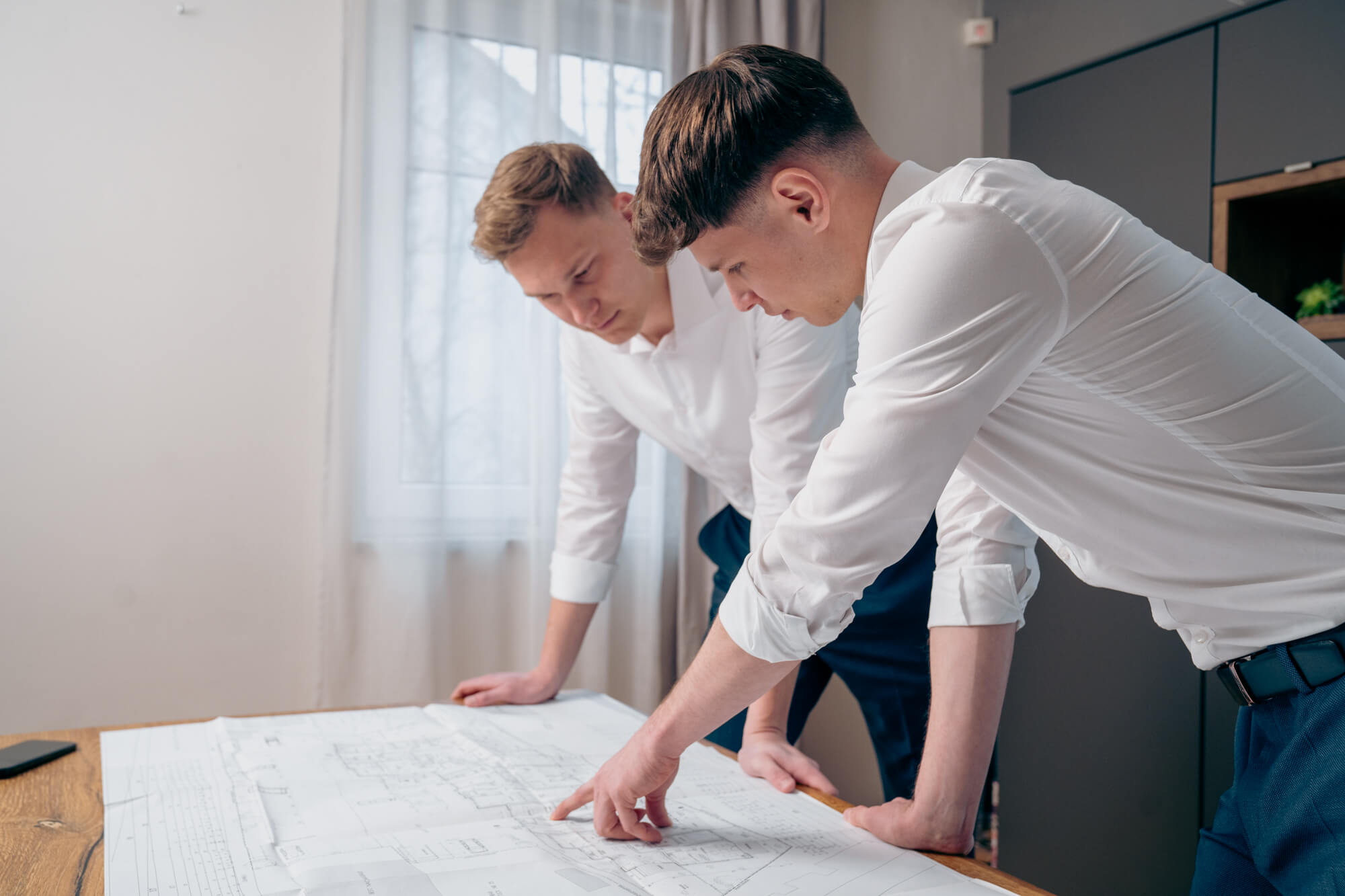 Zwei junge Männer : Jakob Dietl und Nicolas Pfarr beugen sich über ausgebreitete Baupläne und besprechen Details in einem hellen Büro